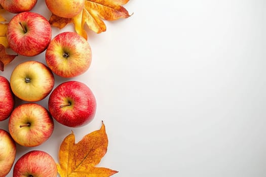 A collection of fresh red and yellow apples is artistically arranged on a pristine white surface, accompanied by vibrant autumn leaves, evoking a sense of seasonal freshness and warmth.