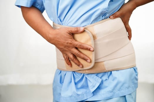 Asian senior pain back wearing elastic support belt with walker.