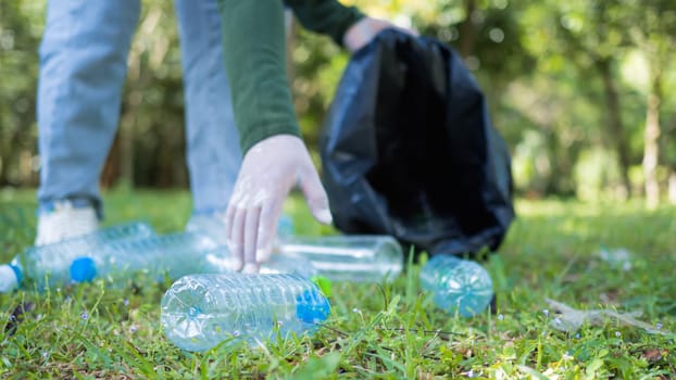 Woman of dedicated volunteers are participating in an environmental cleaning activity in a park. Woman wearing gloves and hold large black bags. Woman collecting trash and plastic bottles in a park.