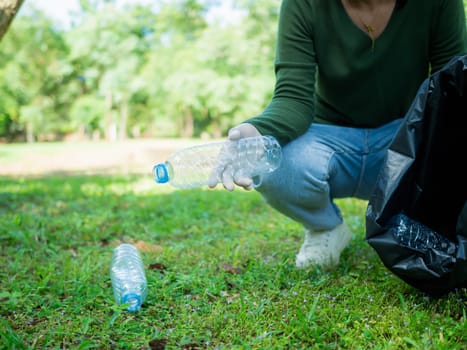 Woman of dedicated volunteers are participating in an environmental cleaning activity in a park. Woman wearing gloves and hold large black bags. Woman collecting trash and plastic bottles in a park.