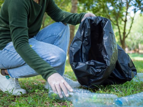 Woman of dedicated volunteers are participating in an environmental cleaning activity in a park. Woman wearing gloves and hold large black bags. Woman collecting trash and plastic bottles in a park.
