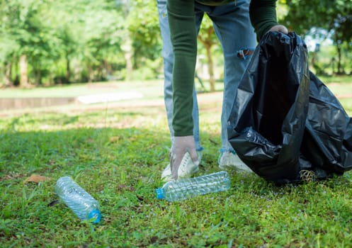 Woman of dedicated volunteers are participating in an environmental cleaning activity in a park. Woman wearing gloves and hold large black bags. Woman collecting trash and plastic bottles in a park.