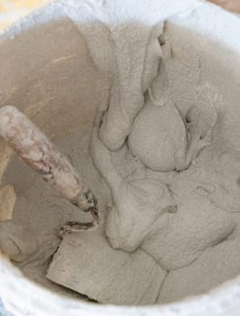 Bucket with cement or plaster on dirty surface with trowel inside, covered in cement residue, top view. Construction or renovation process