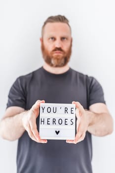 Nurse day concept. Man hands holding lightbox with You are heroes text thanking doctors, nurses and medical staff working in hospitals during coronavirus COVID-19 pandemics.