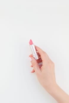 Woman hand with pastel manicure polish holding pink lipstick isolated on white background with copy space. Template for feminine beauty blog social media