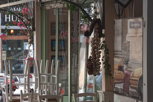 Nicosia, Cyprus - May 22, 2020: White chairs stacked on tables of a traditional cypriot restaurant decorated with hanging garlic and peppers