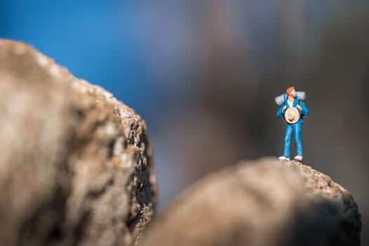 Miniature figure of a hiker standing on a rock with a backpack and a straw hat, deciding which way to go