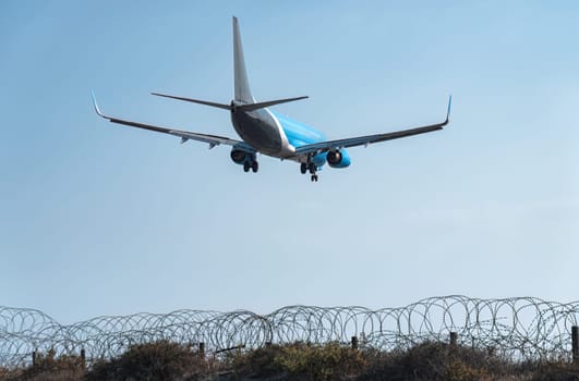 Passenger airplane is landing at an airport behind a barbed wire fence