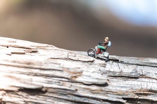 Miniature figurine of a man with a backpack riding a motorcycle on a log is enjoying a sunny day outdoors