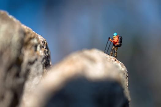 Miniature hiker is reaching the top of a rocky mountain peak, symbolizing determination and the pursuit of goals
