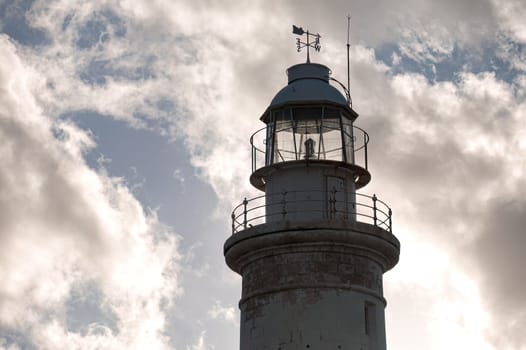 The top of Paphos lighthouse is illuminated by the sun shining through a cloudy sky