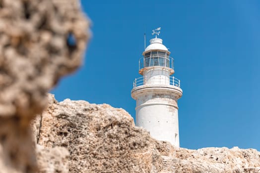 Paphos lighthouse rising high above the rocky coastline on a bright summer day with a clear blue sky. Cyprus