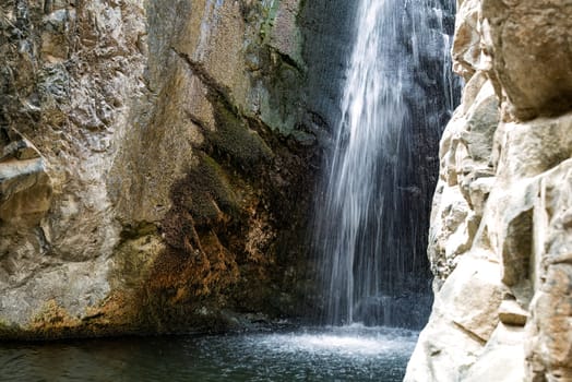Water is falling from the top of a cliff into a pool of water at the Millomeris waterfalls. Cyprus