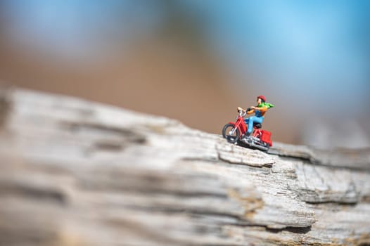Miniature figurine concept of a man riding a moped on a tree trunk