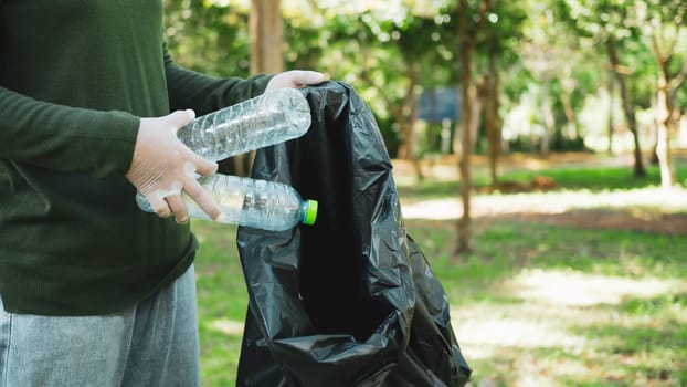 Woman of dedicated volunteers are participating in an environmental cleaning activity in a park. Woman wearing gloves and hold large black bags. Woman collecting trash and plastic bottles in a park.