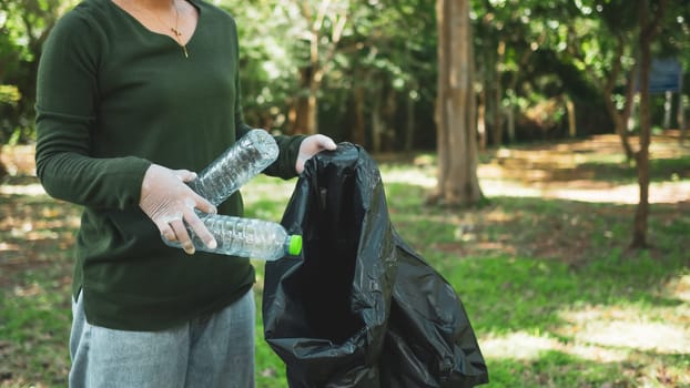 Woman of dedicated volunteers are participating in an environmental cleaning activity in a park. Woman wearing gloves and hold large black bags. Woman collecting trash and plastic bottles in a park.