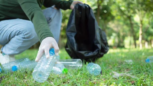 Woman of dedicated volunteers are participating in an environmental cleaning activity in a park. Woman wearing gloves and hold large black bags. Woman collecting trash and plastic bottles in a park.