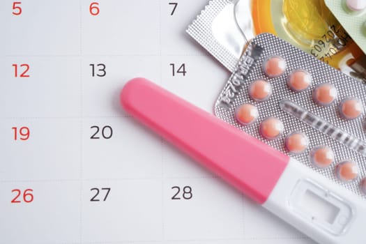 Pregnancy test with birth control pills and condom for female on calendar, ovulation day.