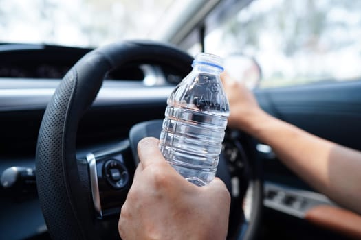 Bangkok, Thailand May 15, 2022 Asian woman driver hold cold water for drink in car, dangerous and risk an accident.
