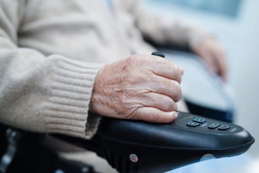 Asian elderly disability woman patient use joystick electric wheelchair in hospital.