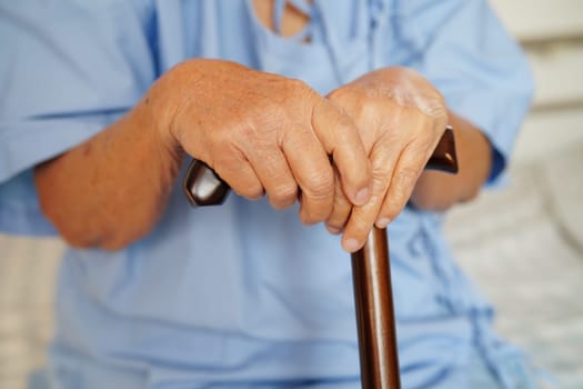 Asian elderly disability woman patient holding walking stick in wrinkled hand at hospital.