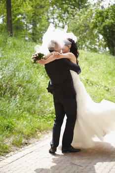 A joyful couple is happily sharing a romantic embrace on their beautiful wedding day outdoors surrounded by nature