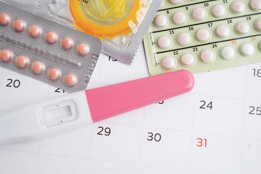 Pregnancy test with birth control pills and condom for female on calendar, ovulation day.