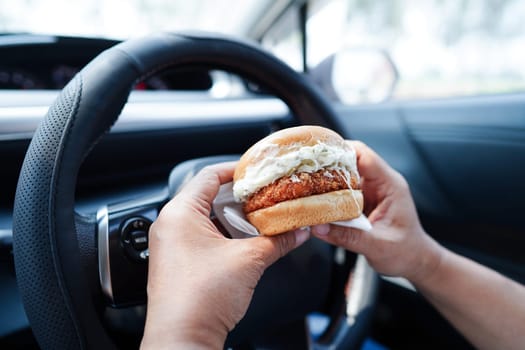 Asian woman driver hold and eat hamburger in car, dangerous and risk an accident.