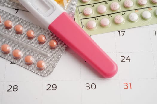 Pregnancy test with birth control pills and condom for female on calendar, ovulation day.