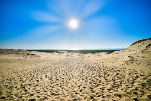 View of bright sun over nordic dunes of Curonian spit, Nida, Klaipeda, Lithuania. Sun rays and sand patterns with a lot of footprints