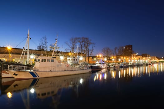 Jetty for boats and yachts in Klaipeda, Lithuania, on sunset. Beautiful view of vessels and their reflections in calm water on blue hour