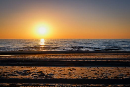 Beautiful view of northern sunset over Baltic sea in Klaipeda, Lithuania. Sun low above calm sea, trails on sand. Concept of calm, quiet contemplation.