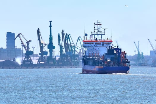 View of commercial cargo port and its container bridge cranes and a ship entering port on a sunny day.