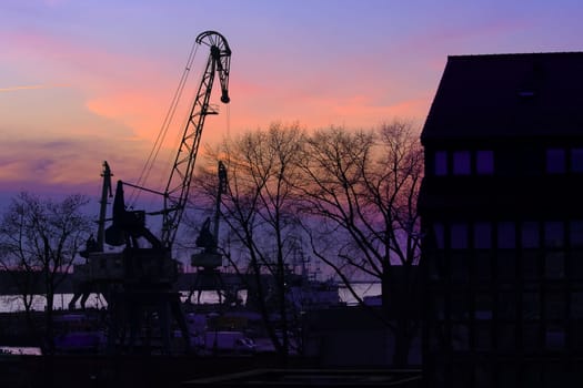 Silhouettes of port crane, trees and building in beautiful colorful sunset in port harbor in Klaipeda, Lithuania.