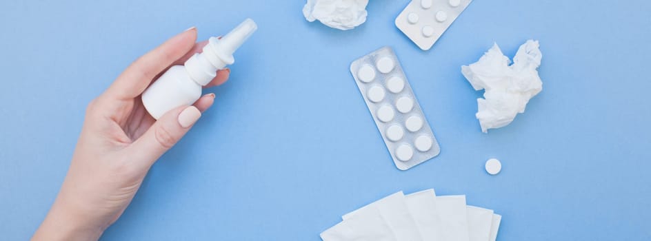 Creative flat lay concept of seasonal spring allergy with napkins, pills, face mask, drops in a bottle and a female hand with copy space long wide banner minimal style, template for text