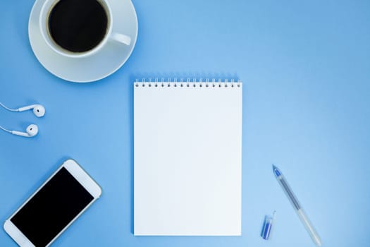 Creative flat lay photo of workspace desk with paper notebook, smartphone, earpieces, pen and coffee with copy space background minimal style