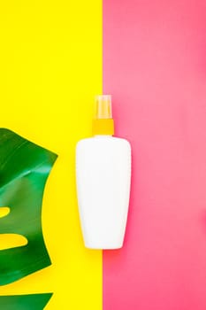 Tropical jungle palm monstera leaves and sunscreen blank bottle mockup on bright yellow and pink duotone paper background. Summer vacations creative flat lay concept template for text