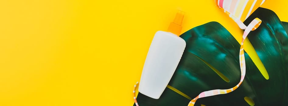 Tropical jungle palm monstera leaves, sunscreen blank bottle mockup and woman's swimsuit on bright yellow paper background. Summer vacations creative flat lay concept template text. Long wide banner