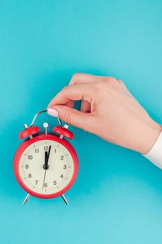 Creative flat lay concept top view of woman hand in white shirt holding the red vintage alarm clock on bright blue turquoise color paper background with copy space in minimal style, template for text