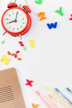 Creative flat lay back to school concept with alarm clock, color school and office supplies on white table background with copy space, frame, template for text or design