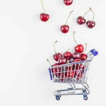 Square image of ripe cherries in a shopping cart with copy space isolated on white background in minimal style. Concept of supermarket or fruit market shopping. Template for your text or design.