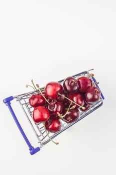 Creative top view of ripe cherries in a shopping cart with copy space isolated on white background in minimal style. Concept of supermarket or fruit market shopping. Template for your text or design.