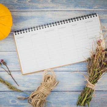 Square Top view of autumn orange pumpkins and dry flowers with grass thanksgiving background over blue toned wooden table with blank timetable mock up and copy space in rustic style, template for text
