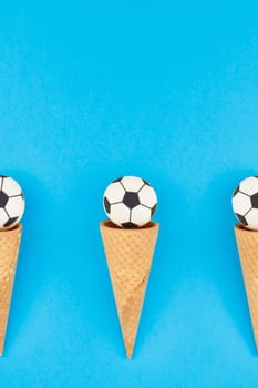 Creative flat lay top view of ice cream waffle cones with soccer balls macarons on bright bold blue background with copy space in minimal style, concept of football games for children birthday