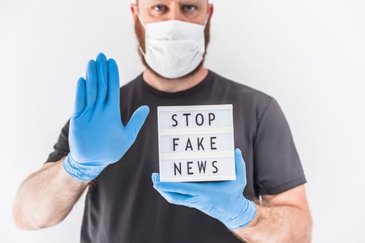 Fake news infodemics during Covid-19 pandemic concept. Man wearing protective mask and medical gloves on hands holding lightbox with text Stop fake news. People want to know truth about coronavirus