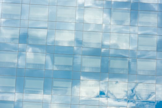 blue sky and clouds reflected in windows of modern office building