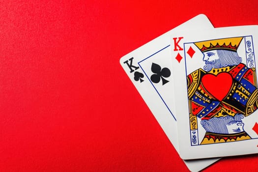 A king of hearts card prominently displayed against a solid bright red background, accompanied by a king of clubs card. This vibrant composition emphasizes the regal design of the playing cards.