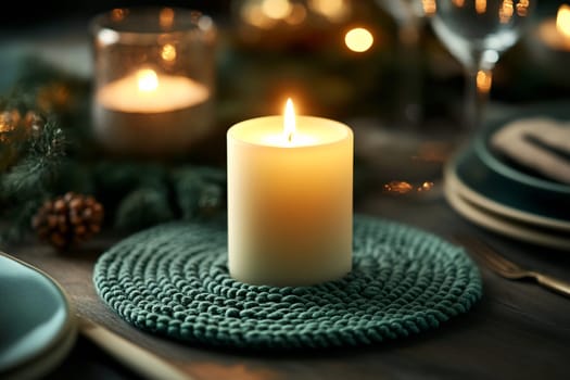 A warm candle casts a soft glow amidst a festive table adorned with greenery and elegant dinnerware, creating a comforting atmosphere.