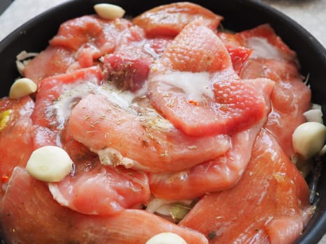 Tender cuts of meat are spiced and arranged for cooking, surrounded by garlic and herbs, creating a savory dish steeped in rich flavors and aromas. Raw meat is soaked in beer for baking in the oven.
