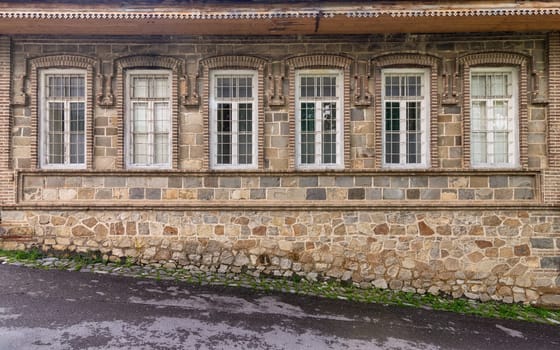This setting features a historic stone building showcasing multiple ornate windows. It reflects classic architectural elements, enveloped by a tranquil village landscape